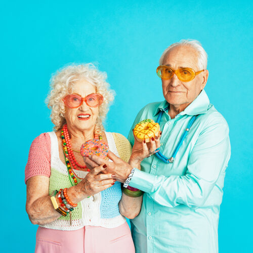 Beautiful senior old couple wearing fancy party clothes acting in studio on a colored background. Conceptual image about third age and seniority, old people feeling young inside.