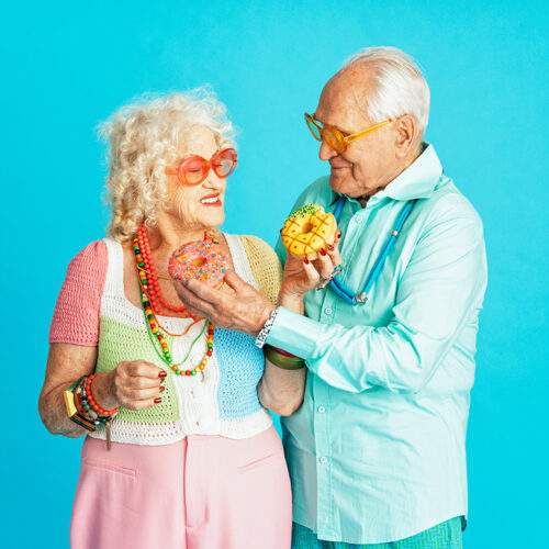 Beautiful senior old couple wearing fancy party clothes acting in studio on a colored background. Conceptual image about third age and seniority, old people feeling young inside.