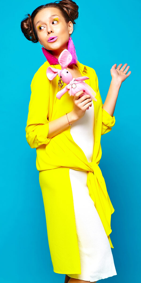 portrait of cheerful fashion hipster girl in casual colorful vivid hipster yellow summer clothes with toy in hands on blue background