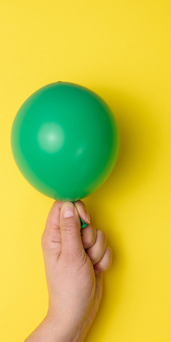 female hand holding an inflated green air balloon on a yellow background, close up