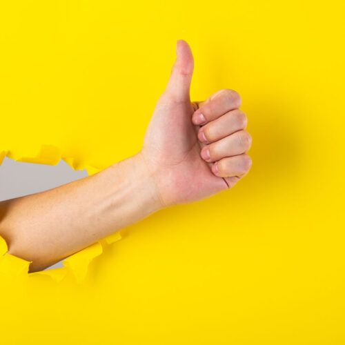 hand-showing-a-thumb-up-sign-through-a-ripped-hole-2023-11-27-04-56-03-utc