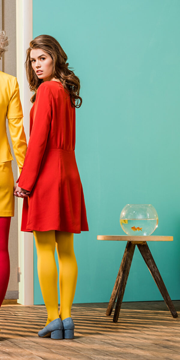 rear view of women in bright retro styled clothing holding hands at colorful apartment, doll house