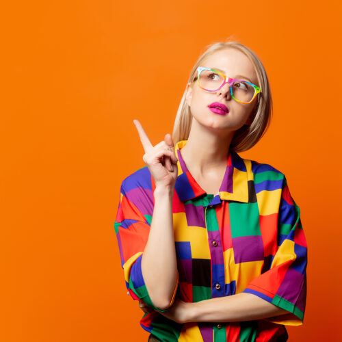 Style blonde in 90s clothes and rainbow glasses on orange background