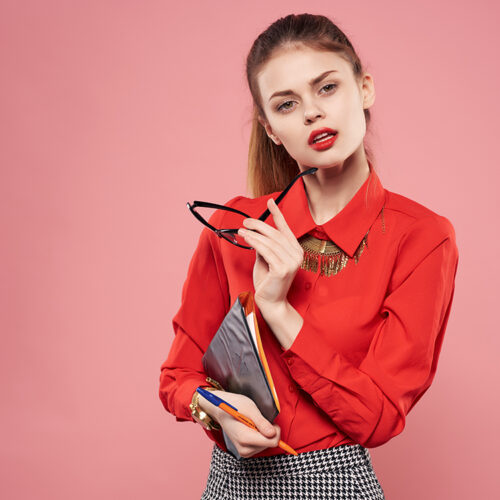 woman in red shirt and glasses documents in hands of secretary pink background. High quality photo
